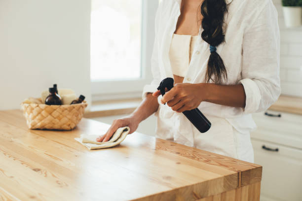 Person wiping a wooden countertop with a cloth and spray bottle, demonstrating a cleaning hack.