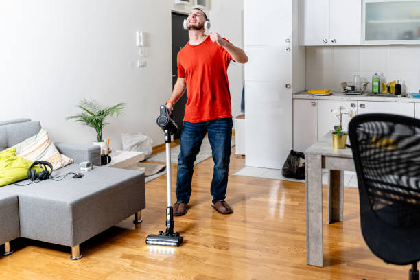 Man joyfully vacuuming hardwood floor with headphones on, highlighting the importance of regular cleaning.